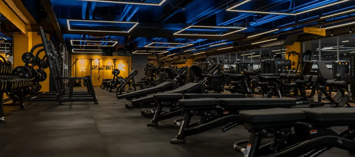 Sala de musculación de una sede Smart Fit con luces azules y paredes amarillas